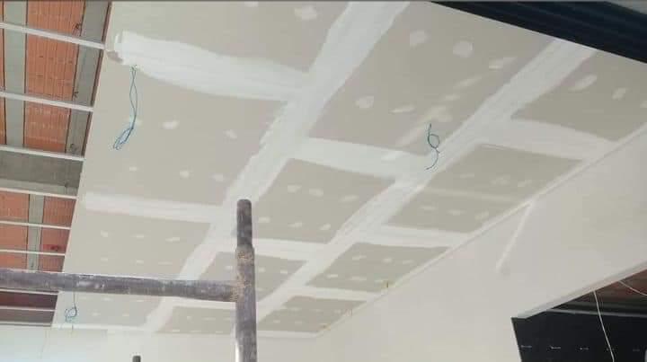 ceiling with drywall panels, white joint compound, and construction elements like metal studs and a scaffold p
