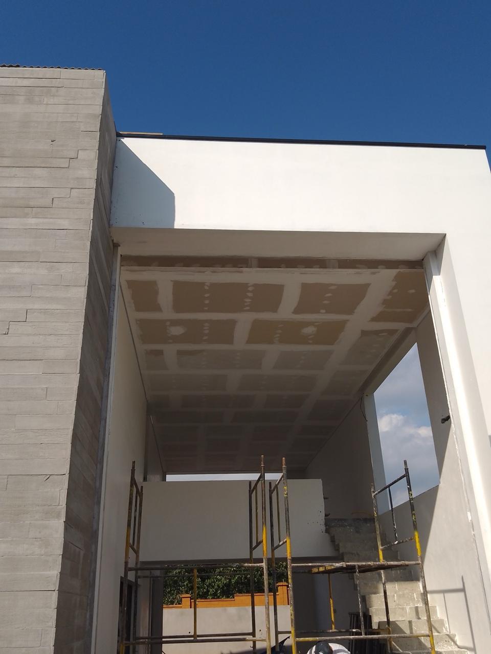Imagem de uma construção em andamento com paredes brancas, tijolos, teto com gesso e uma escada de escoramento
