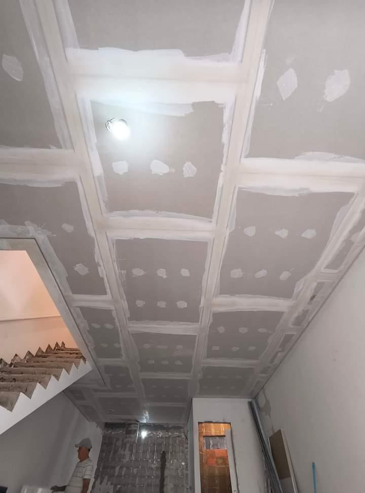 ceiling under construction with drywall panels and joint compound, showing a worker and a staircase