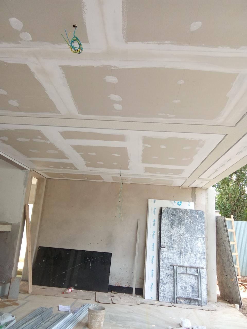 interior de uma construção em andamento com teto de gesso, materiais de obra no chão e paredes em estado bruto