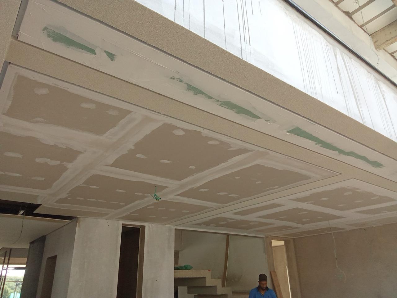 interior de construção com gesso em teto, trabalhador em azul na parte inferior direita
